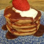 banana pancakes stack with strawberry sauce, yoghurt and a strawberry. On blue plate, wooden surface in background