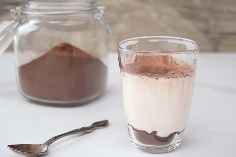 thermomix smilo milo chocolate powder in glass jar in the background on left, right shows a glass of smilo with milk