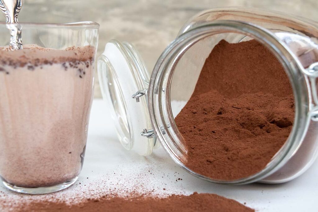 thermomix smilo milo chocolate powder in glass jar on its side on the right, left shows a glass of smilo with milk