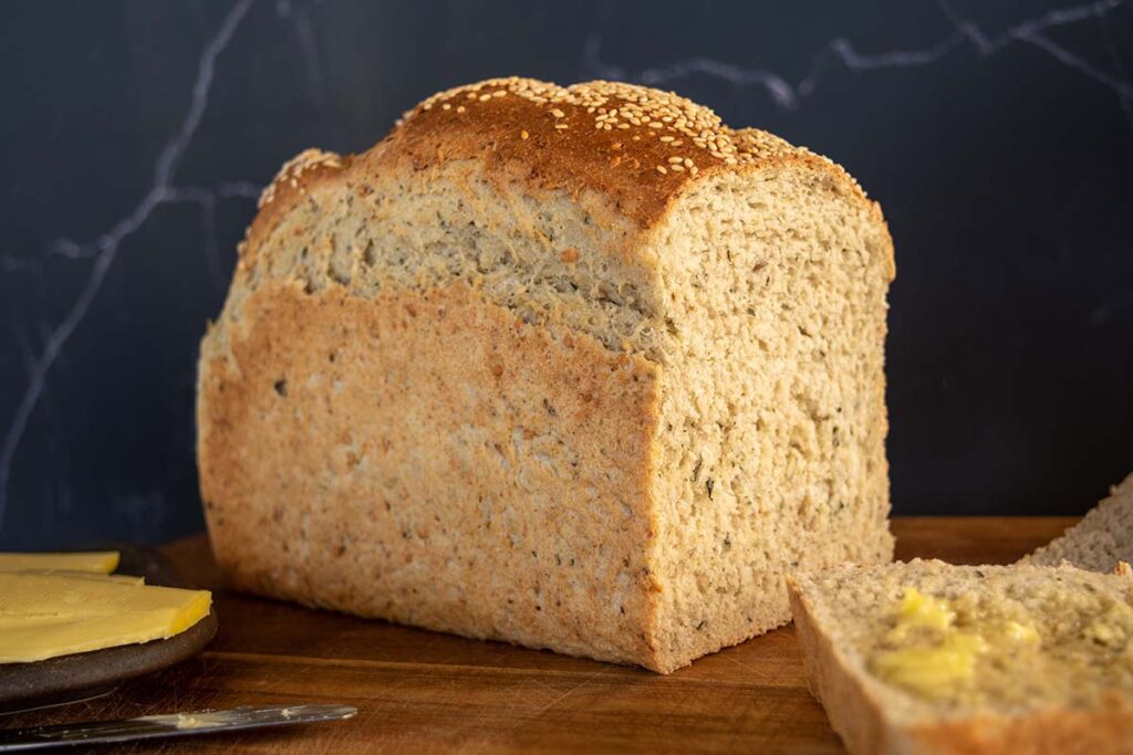 cut loaf side on, super seeded thermomix wholemeal multigrain bread loaf. Black background. Wooden tabletop