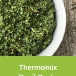 Zoomed in photo of green Thermomix pesto sauce in white bowl, sitting on wooden table