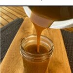 salted caramaple sauce being poured from thermomix jug into jar sitting on wooden board