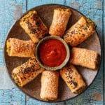 Crackly blue background, brown plate with roast pumpkin fetta rolls in nice pattern with tomato sauce in middle