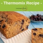 blueberry and lemon loaf on white platter with blueberries in bowl in background on aqua wood table for pin