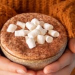 thermomix hot chocolate in mug with marshmallows being held with two hands, person wearing snuggly orange jumper