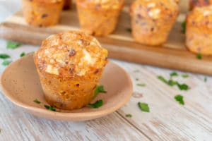 mexi muffins savoury thermomix muffins in background on wooden board, one in foreground on pink plate on white wooden surface scattered with parsley