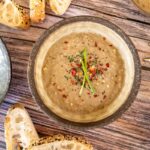 top down photo of a brown bowl of mushroom soup, topped with chilli flakes and chives, parts of two other bowls off to the sides and pieces of turkish bread