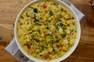 Birdseye view of thermomix vegetable casserole showing a creamy casserole in a white dish, topped with lots of finely chopped parsley. Sitting on a tea towel on a wooden board