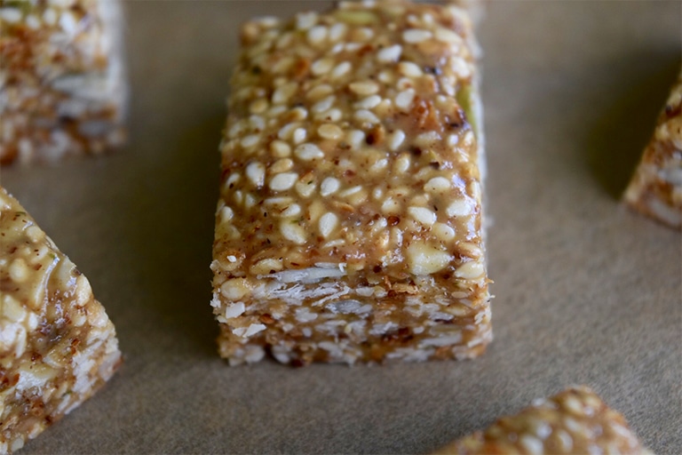 close up of sesame bar on brown parchment paper, corners of four other sesame bars off to the edges of the image.