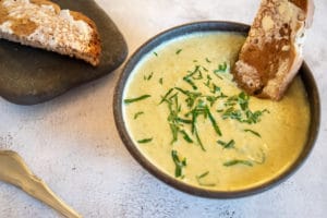 thermomix broccoli soup in black bowl with toast in it and herbs on top, toast in background on black plate. grey background