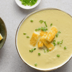 thermomix cauliflower soup in bowl topped with halloumi and chives. White background. Bowl of halloumi and bowl of chives next to soup.