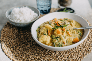 thermomix vegetarian curry in white bowl on straw round placemat with bowl of rice and glass of water in background