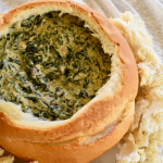 thermomix spinach cob loaf dip in cob loaf. Cream background with chunks of crusty bread around