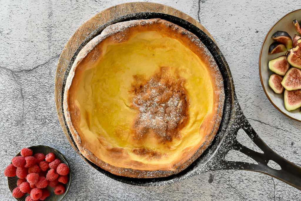 Dutch pancake in cast iron pan on rustic background, with fresh fruit