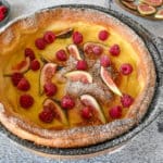 dutch baby pancake in black cast iron pan on rustic background. Fruit inside and outside on plates