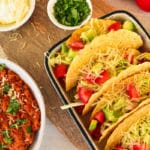 plate of tacos, bowl of taco filling next to it with other ingredients around