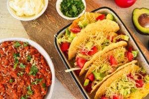 plate of tacos, bowl of taco filling next to it with other ingredients around