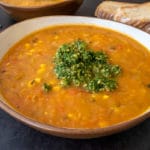 very veggie soup thermomix in bowl with pesto on top, pesto in bowl and toast and another bowl of soup in background. All on black surface.