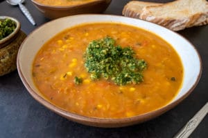 very veggie soup thermomix in bowl with pesto on top, pesto in bowl and toast and another bowl of soup in background. All on black surface.