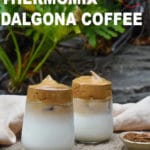 Two cups of milk, dalgona whipped coffee on top. Garden in background, rocks. Small ramekin of coffee.