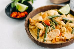 Brown bowl filled with thermomix satay vegetables grey table black bowl with chilli and lime behind