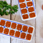 Thermomix tomato paste in ice cube trays and jar on white wood with parsley and tomatoes on vine