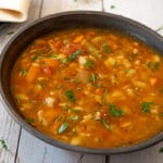 Vegetable soup in black bowl sitting on white wood