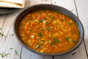 Vegetable soup in black bowl sitting on white wood