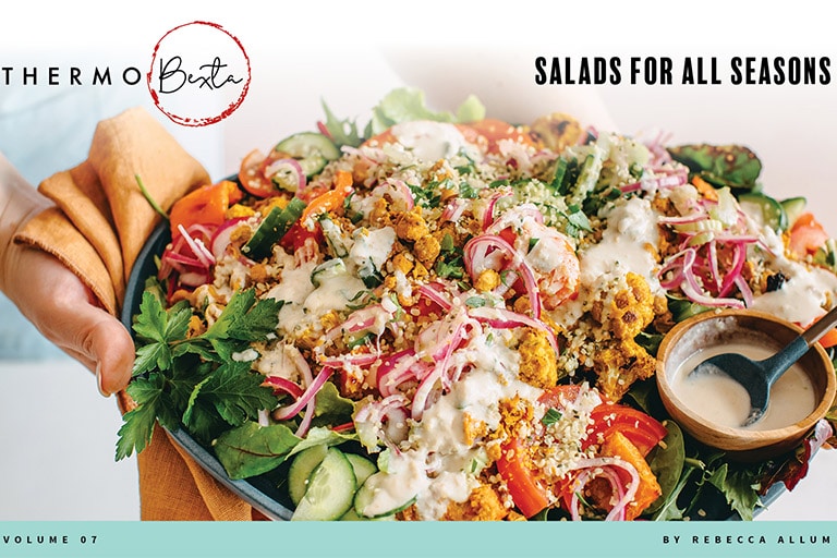 Salad on large platter being held with one hand also holding orange cloth, person in background wearing light blue apron