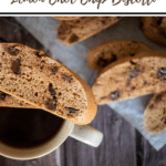 thermomix leeman choc chip biscotti title, Pinterest pin. cup of black coffee with biscotti sitting on top and more in background blurred on wooden backdrop. Brown strip along bottom with Thermobexta logo