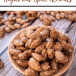 sugar and spice almonds close up of them in a pink dish with some in the background too, on wooden surface, with branding and recipe title for Pinterest