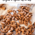 sugar and spice almonds spilling out of a jar onto beige fabric and wooden table, cinnamon sticks top left, with branding and recipe title for Pinterest