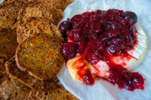 warm brie with Christmas jam sitting on greaseproof paper, with cheese oozing out of part of it. Artesian crackers to the left hand side