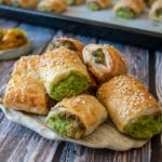 spinach and cheese rolls on rustic cream plate, on wooden table, ramekin of chutney with spoon and tray of more rolls in background