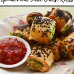 spinach and cheese rolls with black sesame seeds, on antique plate, with ramekin of sweet chilli jam, on green background