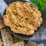 Black leaf shaped dip containing thermomix roasted capsicum dip with crackers underneath and basil leaves above. Pinterest pin.