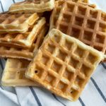 pile of several thermomix waffles laying on striped white and blue tea towel