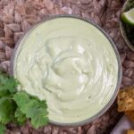 lime coriander cashew sauce in a bowl, on brown placemat. Fresh coriander and lime and corn chips