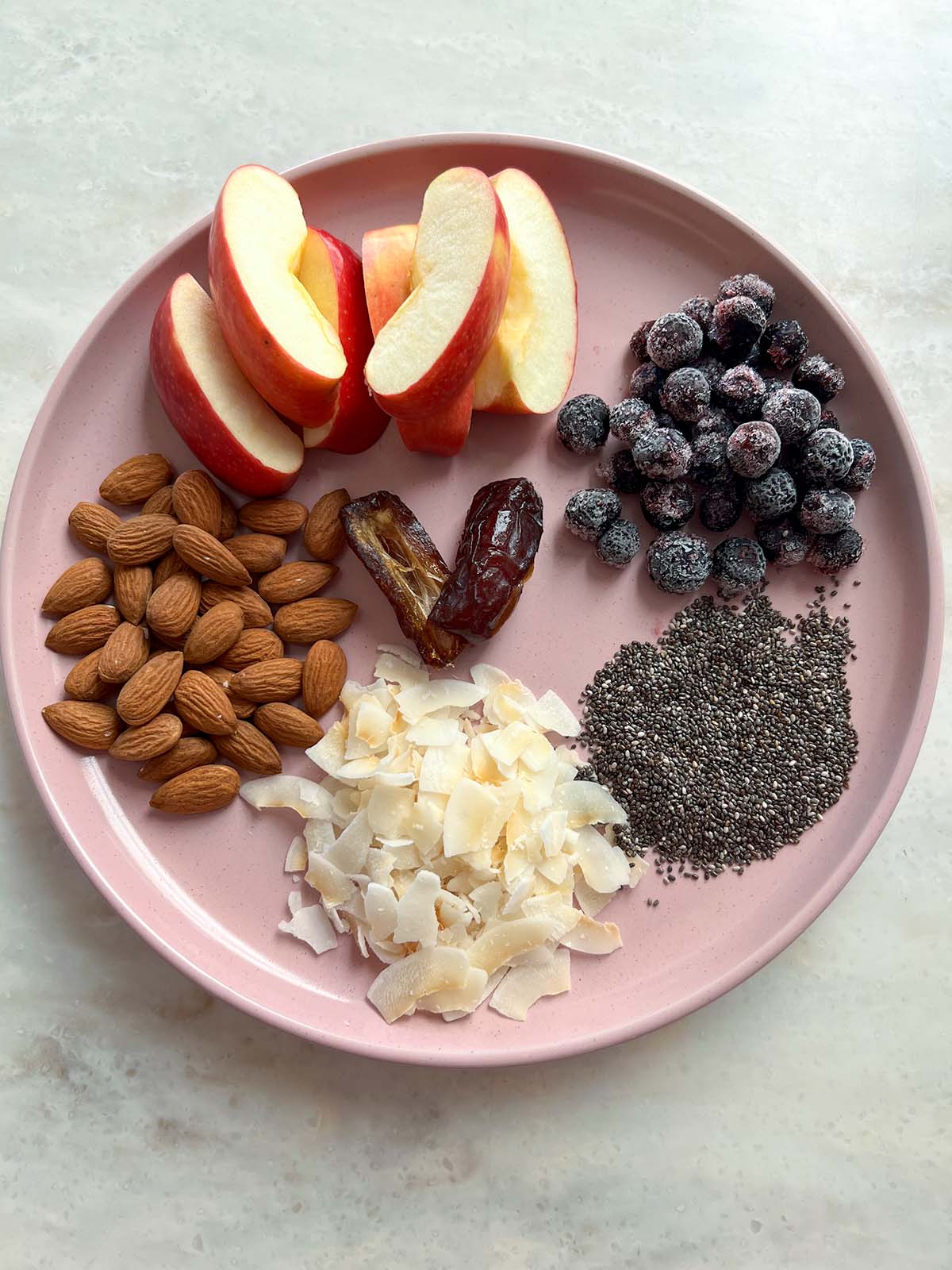 ingredients for fruit and nut breakfast bowls laid out on pink plate on marble countertop