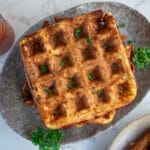 stack of cauliflower cheese savoury waffles on a grey plate. Chilli sauce in a jar above left and part of a plated up waffle bottom right