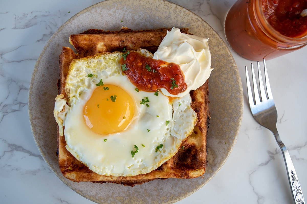 savoury waffle on a plate topped with fried egg, sour cream and chilli sauce