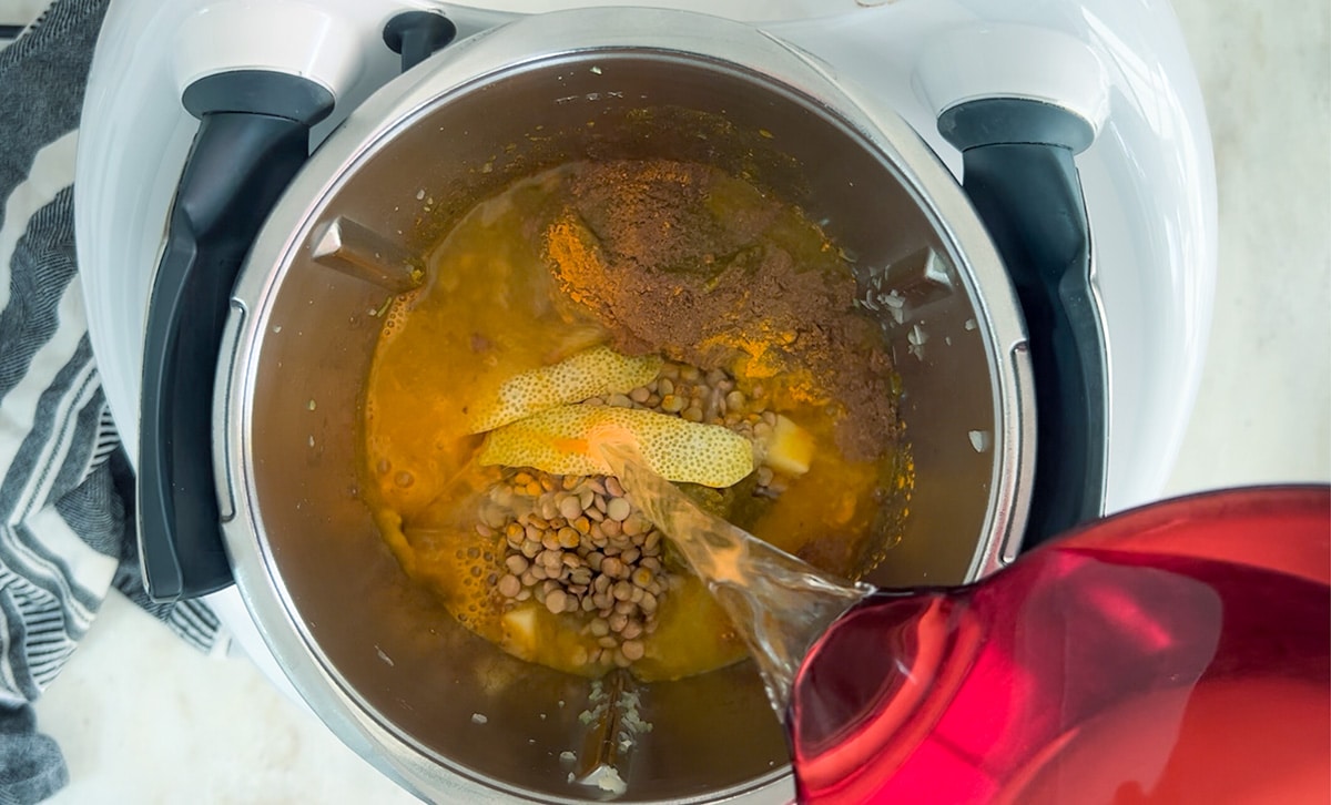 birdseye view into thermomix containing lentil spinach soup ingredients before cooking, water being poured in