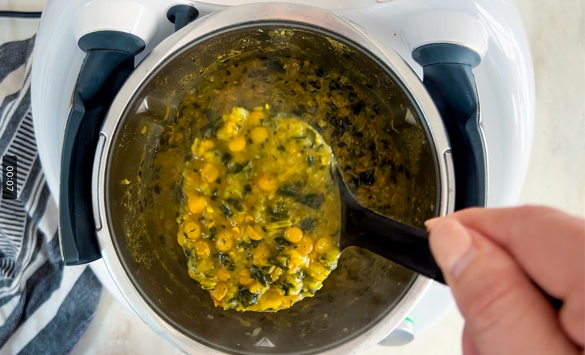 birdseye view into thermomix containing cooked lentil spinach soup, ladel full of soup above bowl