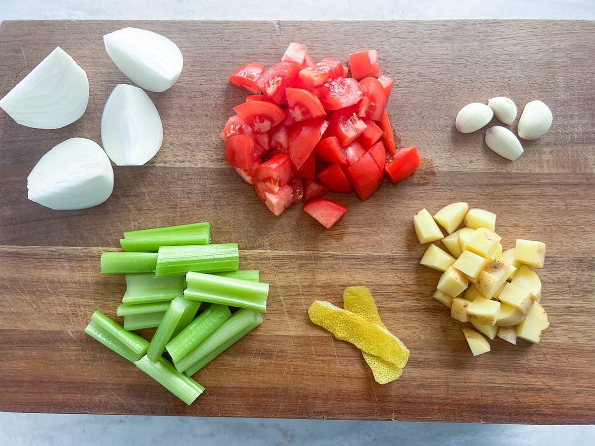 chopped vegetables on brown chopping board for lentil and spinach soup - onion, tomato, garlic, potato, lemon peel, celery