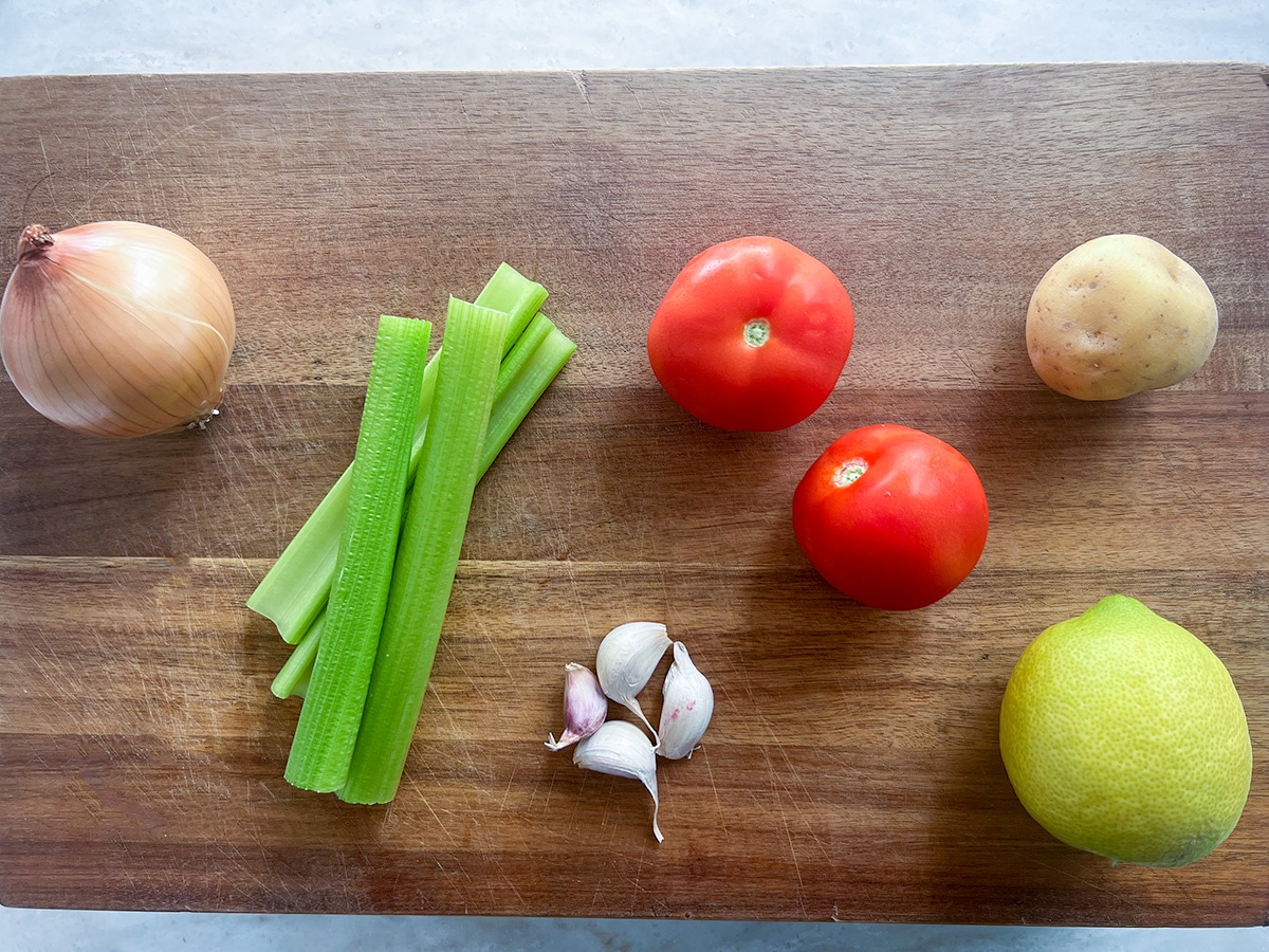 vegetables on brown chopping board for lentil and spinach soup - onion, tomato, garlic, potato, lemon peel, celery