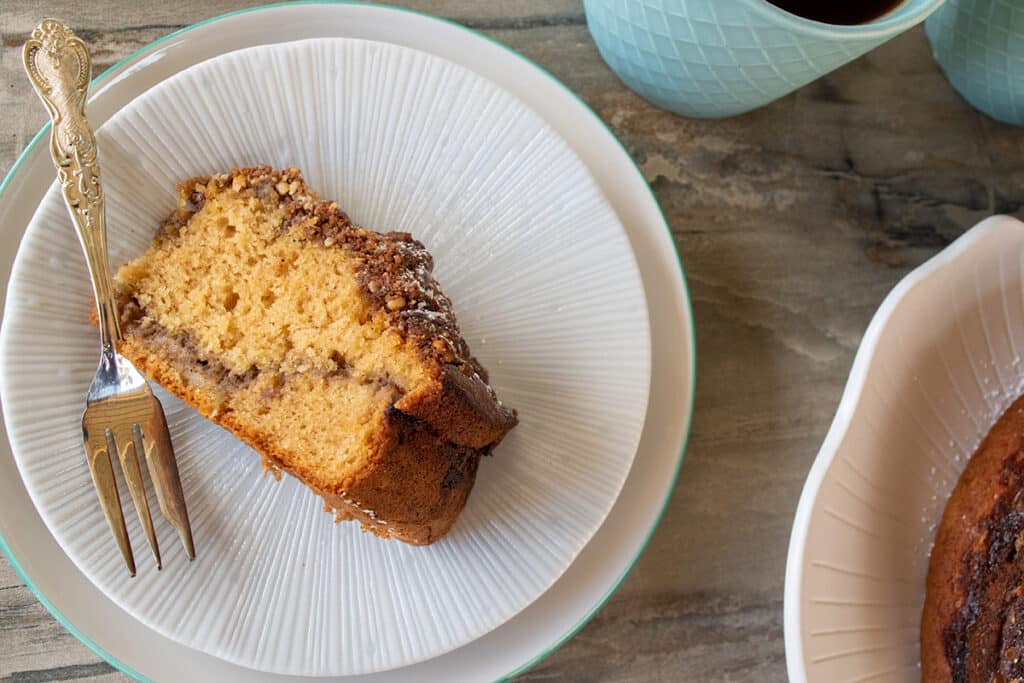 Slice of thermomix cinnamon crumble cake on white plate with fancy cake fork