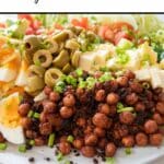 close up of pinterest pin cobb salad on white plate on white surface, chickpeas, olives, eggs, fetta, tomatoes, lettuce, chives