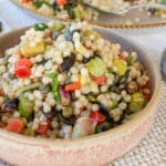 close up of festive couscous salad thermomix in cream and terracotta tapas bowl with spoon to the right. Serving dish containing salad to the back and pistachios between the two dishes