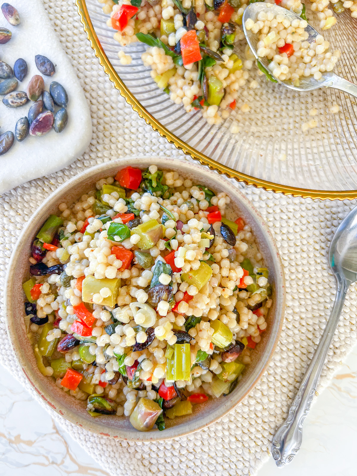 small bowl of festive couscous salad, with spoon and large bowl it's been dished out of