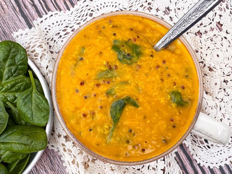 orange coloured pumpkin soup with quinoa and spinach mixed through, in white bowl with handle.